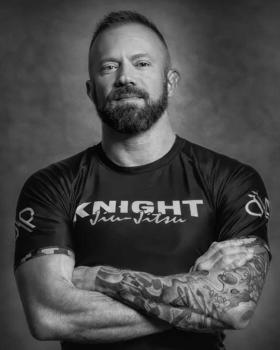 Portrait of Eli Knight with arms crossed wearing a Knight Jiu-Jitsu rashguard, black and white photo.
