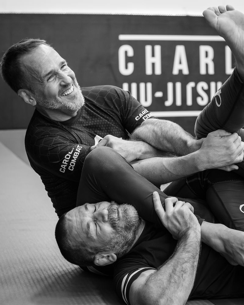 Black and white wall print at Charlotte Jiu-Jitsu Academy: Tom Ziegler armbarring John Piper, both smiling.